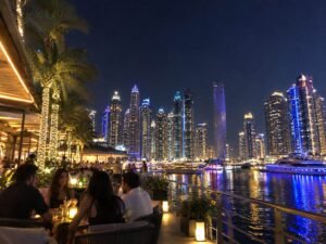 People enjoying dinner and drinks at a licensed outdoor restaurant by the illuminated Dubai Marina at night