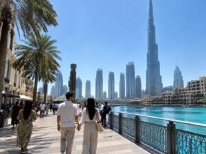 A couple dressed in modest, casual clothing walking along the downtown promenade with the Burj Khalifa in the background